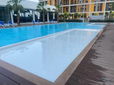 a large swimming pool with blue chairs and a building at Peaceful 2BR with Assistant Room at Mesk 1 Midtown Dubai Production City by Deluxe Holiday Homes in Dubai