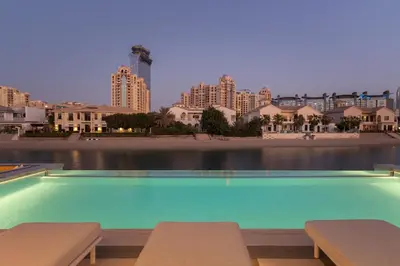 a swimming pool with benches and buildings in the background at Palm Jumeirah Paradise - 5BR Villa - Infinity Pool in Dubai