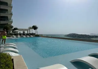 a large swimming pool with white chairs and the ocean at Bright and cozy 1BD apartment on the Beachfront in Dubai