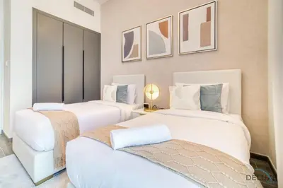 two white beds in a room with paintings on the wall at Exquisite 2BR with Assistant Room at Mesk 1 Midtown Dubai Production City by Deluxe Holiday Homes in Dubai
