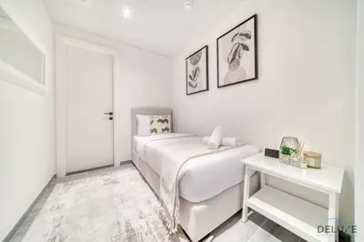 a white bedroom with a bed and a table at Refined 2BR with Assistant Room at Mesk 1 Midtown Dubai Production City by Deluxe Holiday Homes in Dubai
