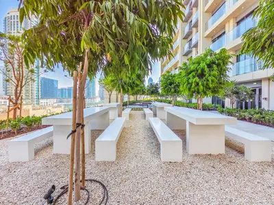 a park with white benches and trees in front of a building at Pleasant 1BR in Burj Royale - Downtown Dubai in Dubai