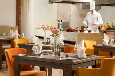 a chef in the kitchen in a restaurant with tables at Carlton Downtown Hotel in Dubai