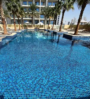 a large blue swimming pool with palm trees and a building at LuxBnB Studio Ghalia J V C in Dubai