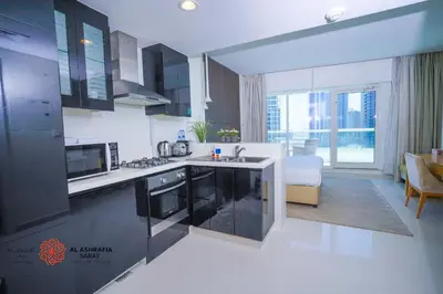 a kitchen with black and white appliances and a living room at Alashrafia Saray- Wonderous Studio in Canal Views in Dubai