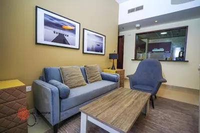 a living room with a couch and a table and a chair at Alashrafia Saray- Homey 1BR apartment in Sport City in Dubai