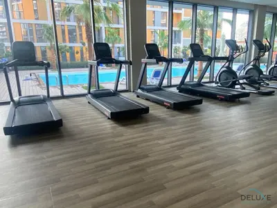 a gym with a row of treadmills and a pool at Classic Studio at Mesk 1 Midtown Dubai Production City by Deluxe Holiday Homes in Dubai