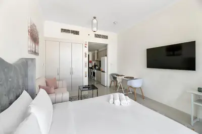 a bedroom with a white bed and a living room at Luxurious - Studio - Damac Hills - Pool & Gym in Dubai