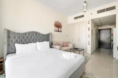a bedroom with a large white bed and a chair at Luxurious - Studio - Damac Hills - Pool & Gym in Dubai