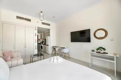 a white bedroom with a bed and a living room at Luxurious - Studio - Damac Hills - Pool & Gym in Dubai