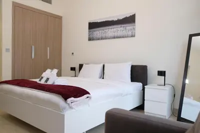 a bedroom with a white bed with a red blanket on it at Mira Holiday Homes - Cozy studio in Meydan in Dubai