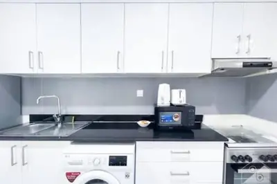a white kitchen with a sink and a microwave at Cozy Spacious Studio With Balcony Dubai in Dubai
