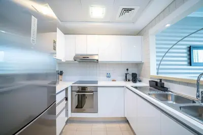 a white kitchen with white cabinets and a sink at Beachfront 1 Bed with Full JBR View in Dubai