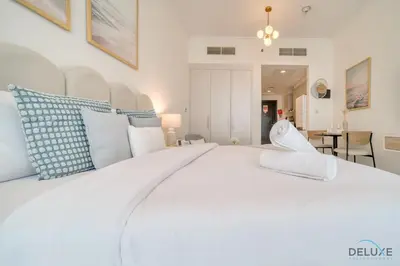 a large white bed with blue and white pillows at Opulent Studio at Carson C DAMAC Hills Dubailand by Deluxe Holiday Homes in Dubai