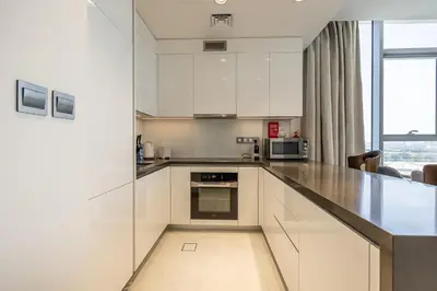 a kitchen with white cabinets and a large window at Fully Furnished I Lagoons View I District One in Dubai