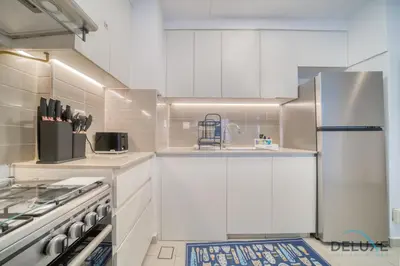 a white kitchen with white cabinets and a refrigerator at Soothing 1BR at Safi 1B Town Square Dubailand by Deluxe Holiday Homes in Dubai