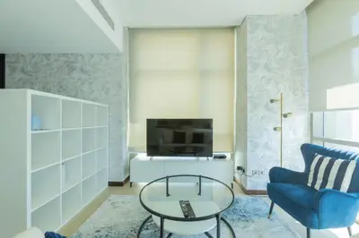 a living room with a blue chair and a tv at Nasma Luxury Stays - White Haven Studio With Charming Cityscape Views in Dubai
