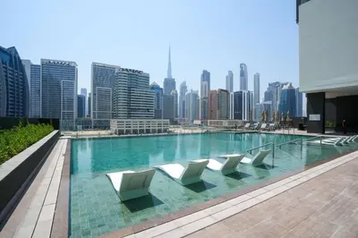 a swimming pool with white chairs and a city skyline at Studio in heart of Dubai - 15 Northside - Business Bay in Dubai