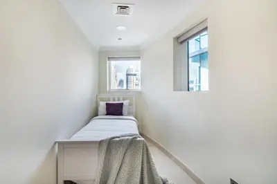a small bed in a white room with a window at The Smart Concierge - Marinascape Oceanic in Dubai