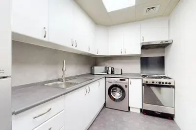 a white kitchen with a washing machine and a sink at V3 Tower - Elegant One Bedroom in Dubai