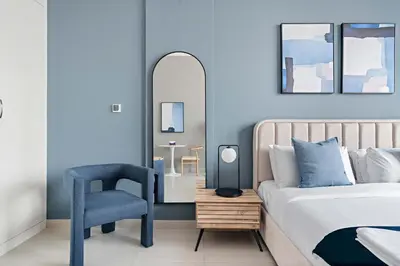 a bedroom with a bed and a chair and a mirror at Silkhaus new studio in Art Gardens pool access in Dubai