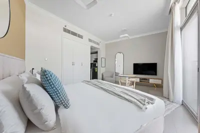 a white bedroom with a bed and a tv at Silkhaus new studio in Art Gardens gym & pool access in Dubai
