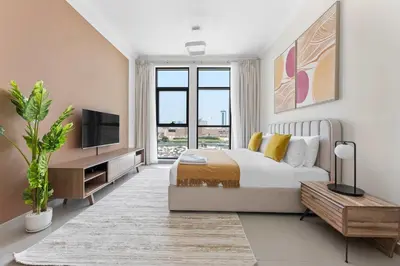 a white bedroom with a bed and a tv and a table at Silkhaus exquisite studio in Art Gardens with gym access in Dubai