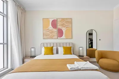 a white bedroom with a large bed and a chair at Silkhaus exquisite studio in Art Gardens with gym access in Dubai