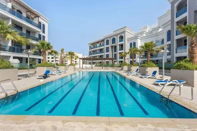 a swimming pool with chairs and a building at Silkhaus exquisite studio in Art Gardens with gym access in Dubai