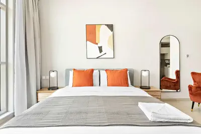 a bedroom with a large bed with orange pillows at Silkhaus furnished studio in Art Gardens with pool access in Dubai