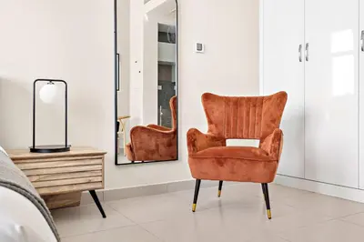 a orange chair in a bedroom with a mirror at Silkhaus furnished studio in Art Gardens with pool access in Dubai