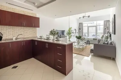 a kitchen with wooden cabinets and a living room at Frank Porter - Oasis Tower 1 in Dubai