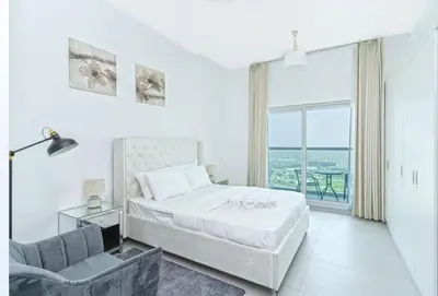 a white bedroom with a bed and a chair at Modern Studio with Pool & Gym Access in Dubai