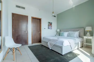 a white bedroom with a bed and a chair at Frank Porter - South Ridge 6 in Dubai