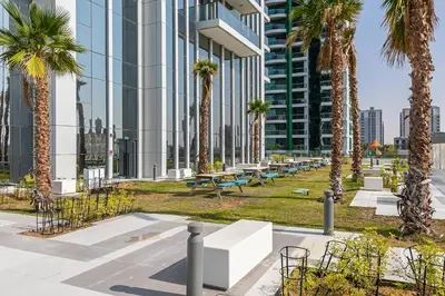 a park with palm trees and benches in front of a building at Stunning 1 Bedroom Apartment - Regina Tower - JVC in Dubai