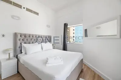 a white bedroom with a large bed and a window at Stunning Lake View - Height Floor - Furnished 1BR in Dubai