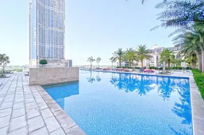 a swimming pool with palm trees and a tall building at bnbme - Luxury 2BR Business Bay Apt w Canal Views Pool Gym Free Parking Downtown in Dubai