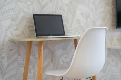 a laptop computer sitting on a wooden table with a white chair at Spacious Serene Studio Retreat in JVC by Suiteable in Dubai