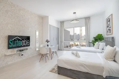 a white bedroom with a bed and a living room at Spacious Serene Studio Retreat in JVC by Suiteable in Dubai