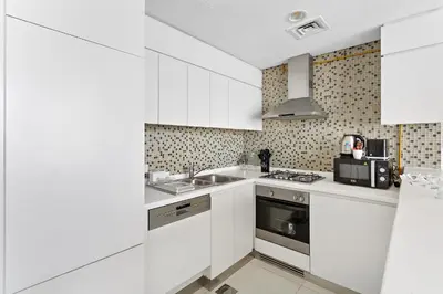 a white kitchen with a sink and a stove at Chic 1BR Apt with Sofa Bed, Pool & Burj Khalifa View in Dubai