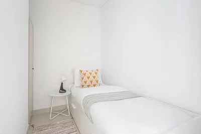 a white bed in a white room with a side table at Frank Porter - The Grand in Dubai