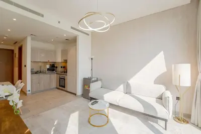 a living room with a white couch and a kitchen at EasyGo - Sobha Waves 1 Bedroom & Study Modern in Dubai