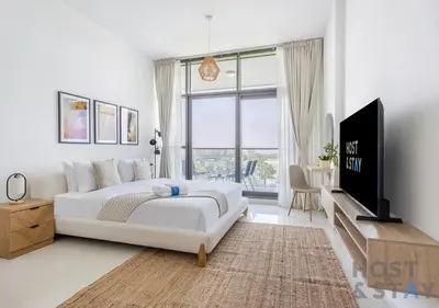 a white bedroom with a large bed and a tv at Studio in Jasmine, Damac Hills - Host & Stay in Dubai