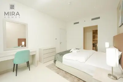 a white bedroom with a bed and a blue chair at Mira Holiday Homes - Lovely 1 bedroom with beach access in Dubai