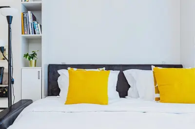 a white bed with yellow pillows on it at Waves Holiday Homes - Chic Studio With Balcony Overlooking City Views in Dubai
