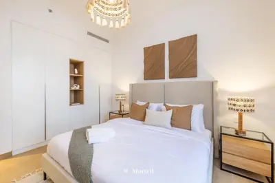 a bedroom with a large white bed and a chandelier at Manzil - 1BR Home in Port de la Mer w Lake Access in Dubai