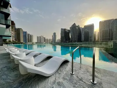 a swimming pool with white chairs in front of a city at Oraya - Studio With Jaw-Dropping Canal and Burj Views - Business bay in Dubai