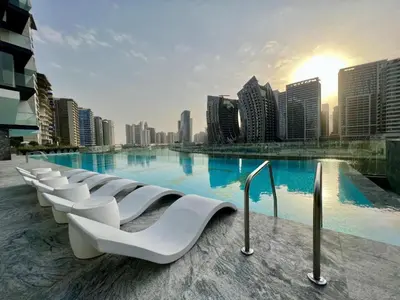 a large swimming pool with white chairs in front of a city at Oraya - Studio With Jaw-Dropping Canal and Burj Views - Business bay in Dubai