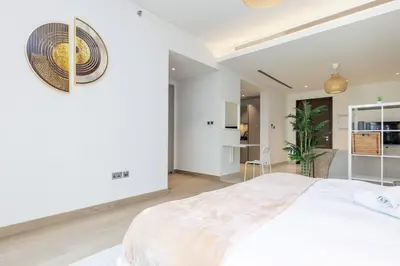 a white bedroom with a large bed and a kitchen at Spacious Minimalistic Studio in Dubai