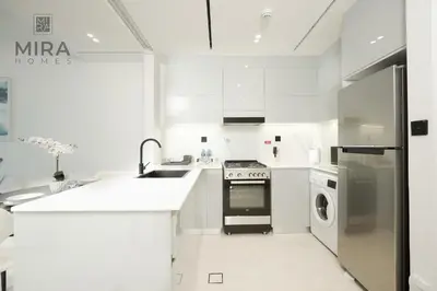 a white kitchen with a sink and a dishwasher at Mira Holiday Homes - Serviced 1 bedroom with canal view in Dubai
